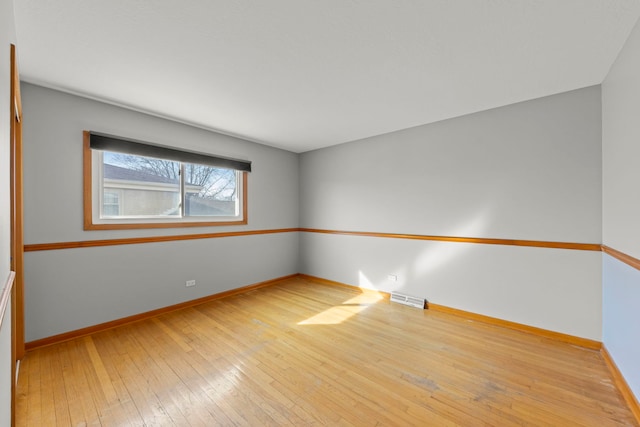 unfurnished room featuring wood-type flooring, visible vents, and baseboards