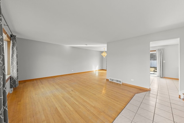 spare room featuring light wood-style floors, baseboards, visible vents, and a notable chandelier