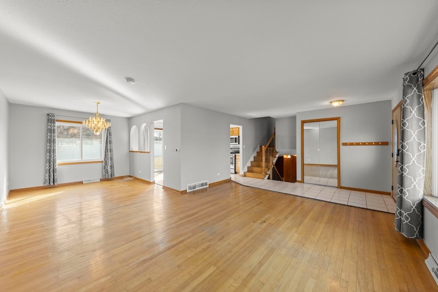 unfurnished living room with visible vents, baseboards, wood-type flooring, stairway, and a notable chandelier