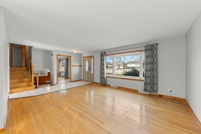 unfurnished living room with visible vents, stairway, baseboards, and wood finished floors