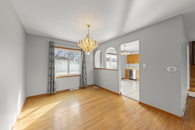 empty room featuring light wood-type flooring, visible vents, a notable chandelier, and baseboards