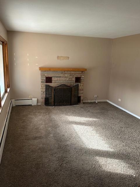 unfurnished living room with a baseboard heating unit, dark colored carpet, and a fireplace