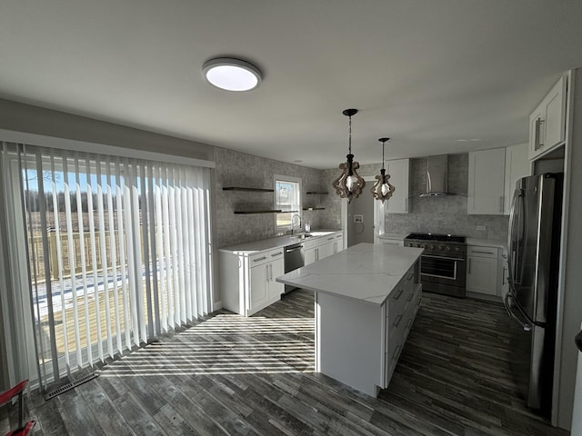 kitchen with wall chimney range hood, white cabinetry, hanging light fixtures, stainless steel appliances, and a kitchen island