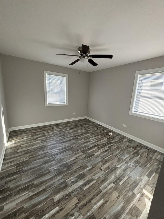 empty room with plenty of natural light, dark wood-type flooring, and ceiling fan