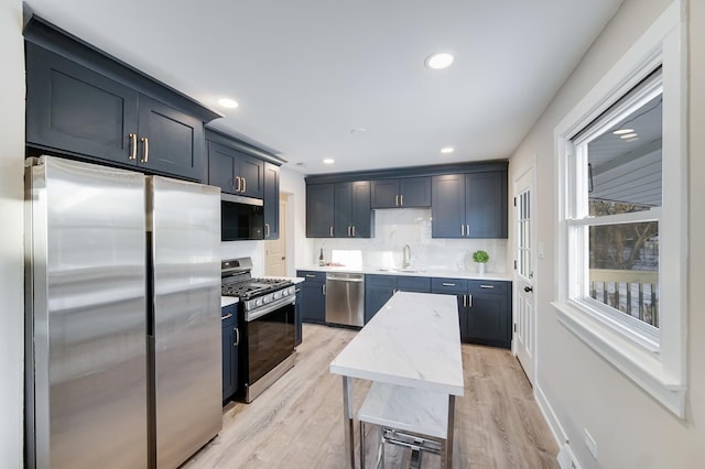 kitchen featuring stainless steel appliances, backsplash, light wood-type flooring, light stone countertops, and sink