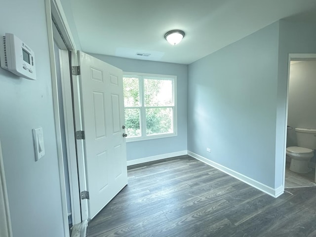 unfurnished bedroom with ensuite bathroom and dark hardwood / wood-style flooring