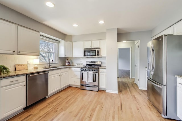 kitchen with appliances with stainless steel finishes, white cabinetry, light wood-type flooring, and a sink