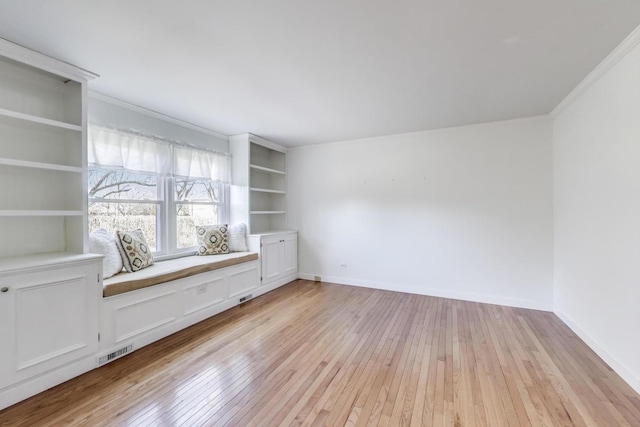 spare room with built in features, baseboards, visible vents, light wood finished floors, and ornamental molding