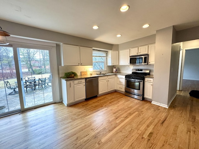 kitchen with a sink, appliances with stainless steel finishes, light wood-style flooring, and white cabinetry