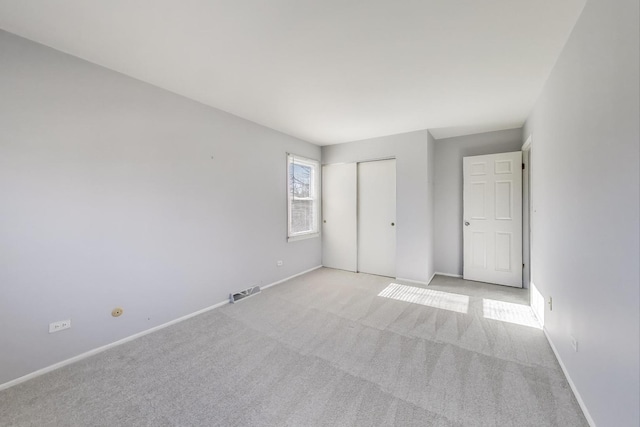 unfurnished bedroom featuring light carpet, visible vents, a closet, and baseboards