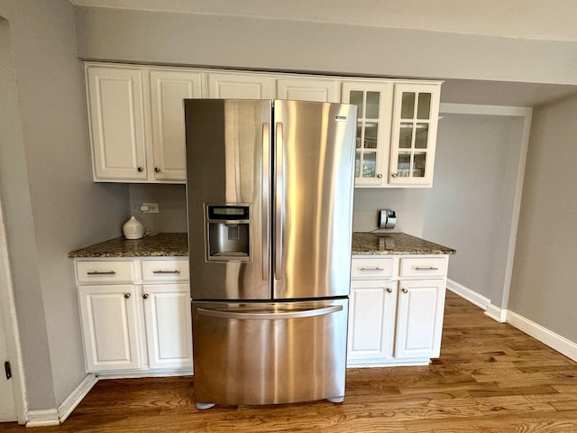 kitchen featuring dark stone counters, glass insert cabinets, stainless steel refrigerator with ice dispenser, and wood finished floors