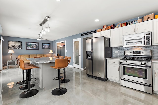 kitchen with a breakfast bar area, white cabinetry, appliances with stainless steel finishes, pendant lighting, and backsplash