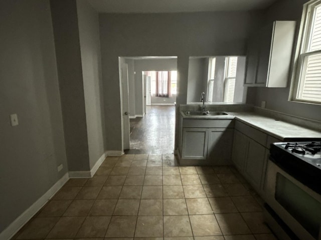 kitchen with sink, light tile patterned floors, gray cabinetry, and gas range