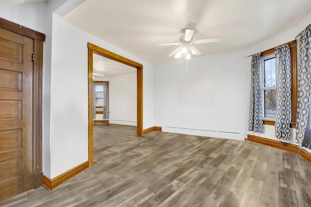 empty room featuring ceiling fan, baseboard heating, and wood-type flooring