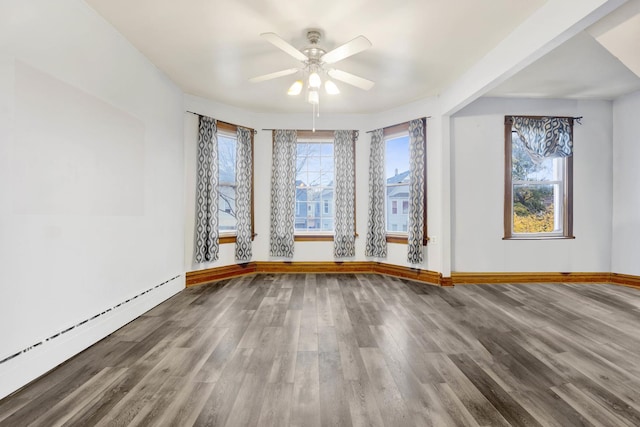 empty room with ceiling fan, baseboard heating, a wealth of natural light, and hardwood / wood-style flooring