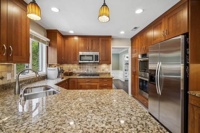 kitchen with light stone countertops, pendant lighting, stainless steel appliances, sink, and backsplash