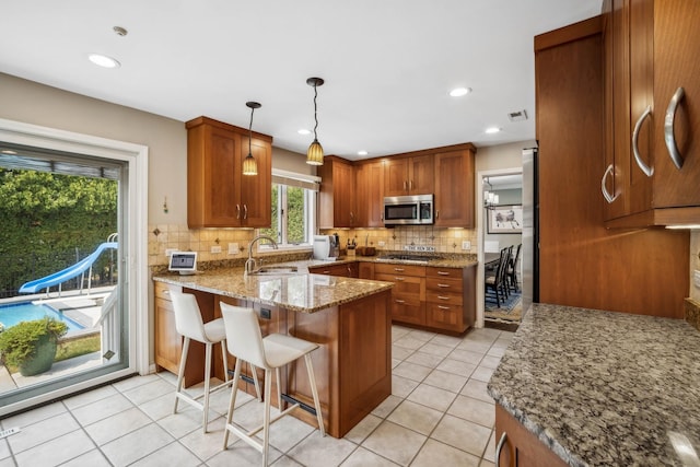 kitchen with kitchen peninsula, a breakfast bar area, appliances with stainless steel finishes, pendant lighting, and sink