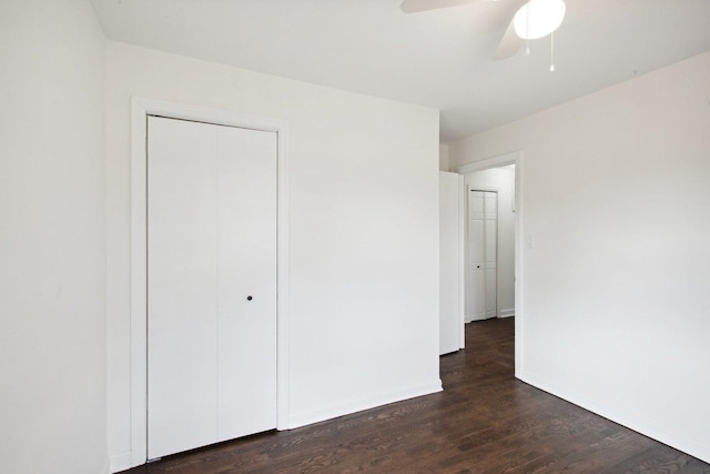 unfurnished bedroom with dark wood-style floors, ceiling fan, a closet, and baseboards