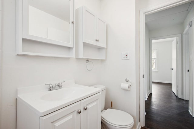 bathroom featuring toilet, baseboards, wood finished floors, and vanity