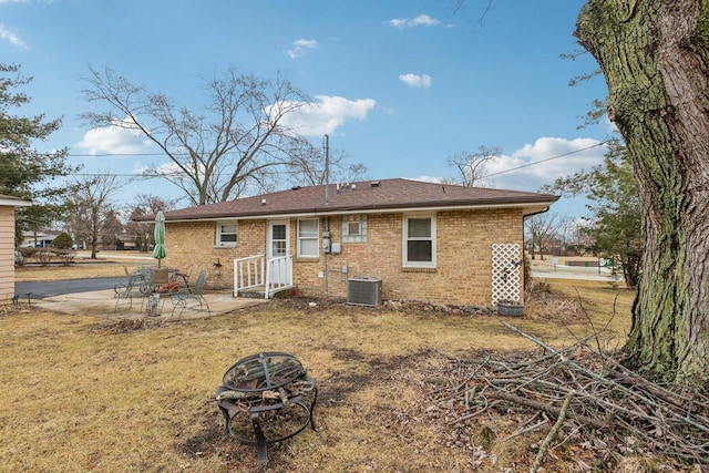 rear view of house with brick siding, a lawn, a patio area, cooling unit, and a fire pit