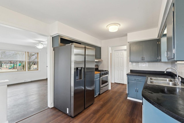 kitchen with dark countertops, appliances with stainless steel finishes, dark wood-type flooring, a sink, and backsplash