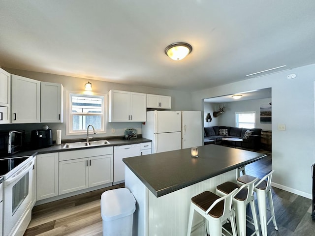 kitchen featuring white cabinetry, sink, a kitchen bar, and white appliances