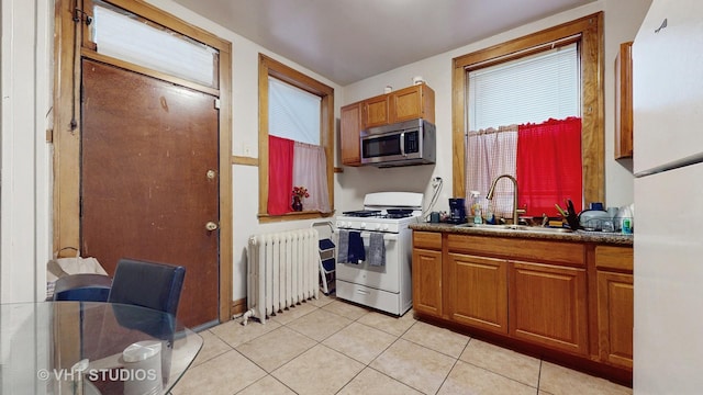 kitchen featuring white range with gas cooktop, sink, light tile patterned floors, and radiator heating unit