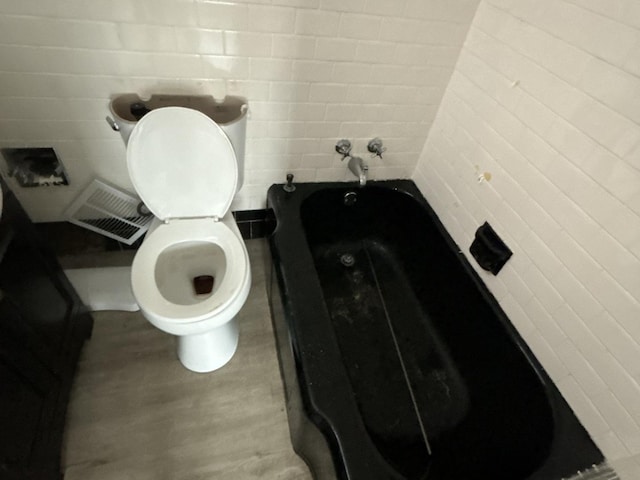 bathroom with a tub to relax in, toilet, tile walls, and wood-type flooring