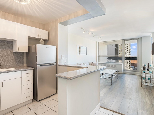 kitchen with white cabinets, sink, backsplash, kitchen peninsula, and stainless steel refrigerator