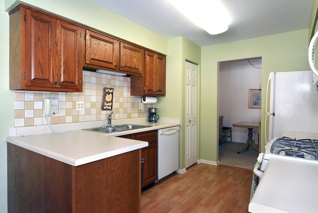 kitchen featuring sink, white appliances, decorative backsplash, kitchen peninsula, and light wood-type flooring