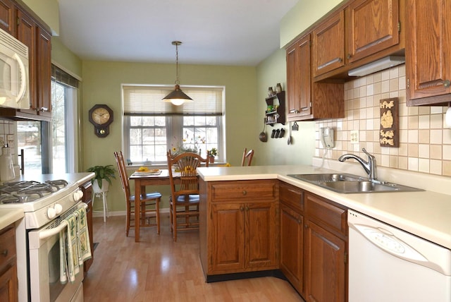 kitchen featuring pendant lighting, sink, white appliances, light hardwood / wood-style flooring, and kitchen peninsula