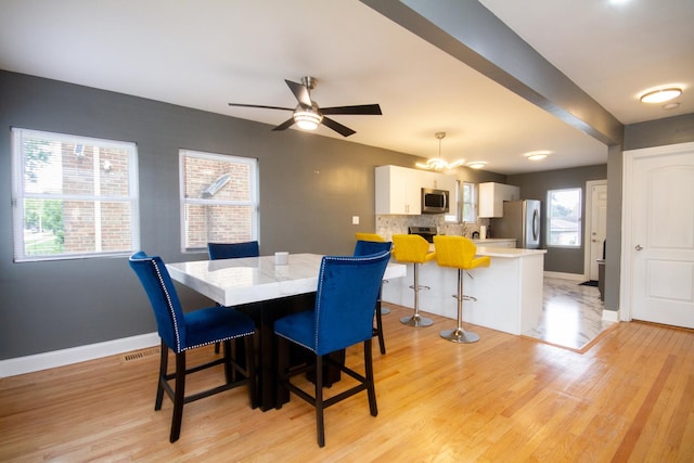 dining room featuring light wood-type flooring, a wealth of natural light, and ceiling fan with notable chandelier