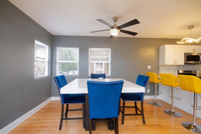 dining room with ceiling fan with notable chandelier and light hardwood / wood-style flooring