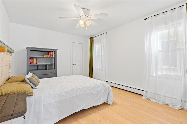 bedroom with a baseboard heating unit, ceiling fan, and wood-type flooring