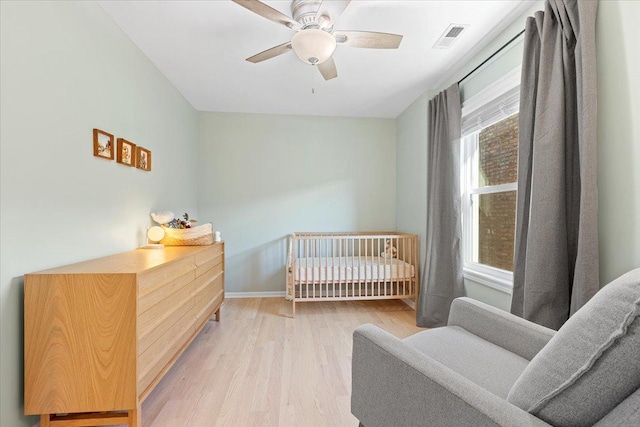 bedroom featuring ceiling fan, a crib, and light hardwood / wood-style floors