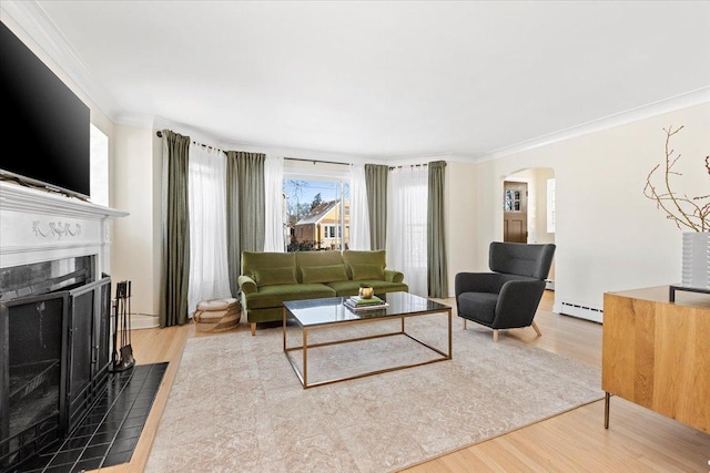 living room featuring hardwood / wood-style flooring, a baseboard heating unit, a tile fireplace, and ornamental molding