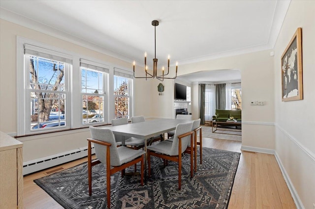 dining space featuring baseboard heating, light hardwood / wood-style flooring, crown molding, and a notable chandelier