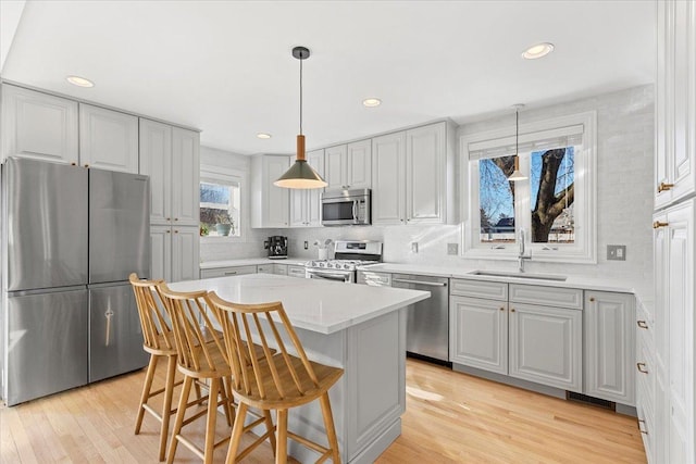 kitchen with decorative light fixtures, a kitchen island, a kitchen bar, sink, and appliances with stainless steel finishes