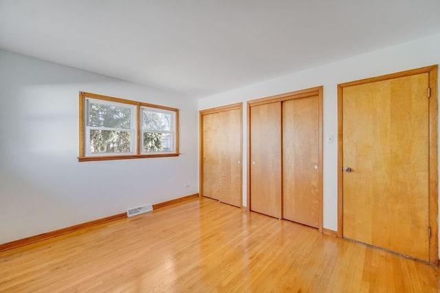 unfurnished bedroom with light hardwood / wood-style floors and two closets