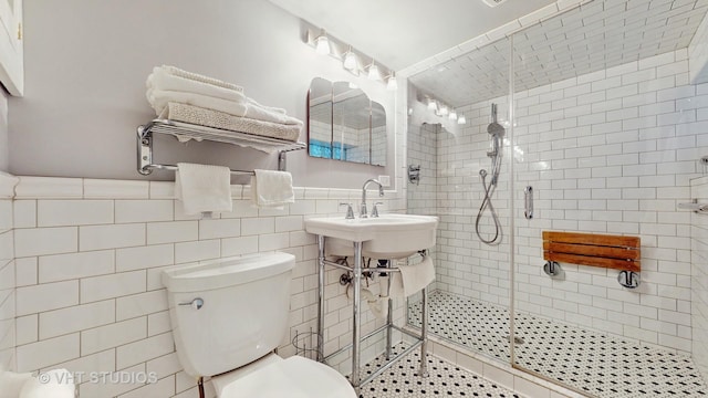 bathroom with toilet, an enclosed shower, sink, and tile walls