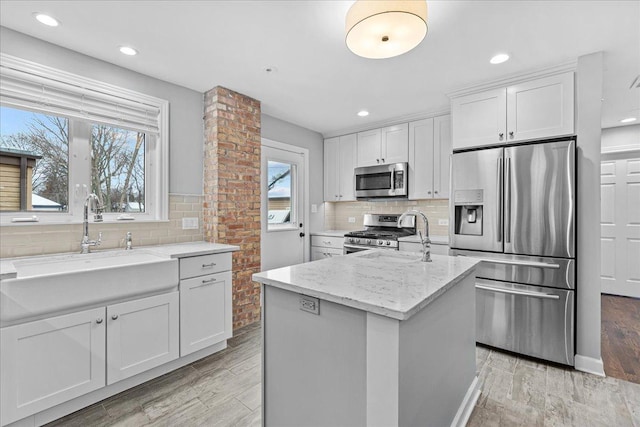 kitchen featuring a center island, white cabinetry, stainless steel appliances, sink, and light stone counters