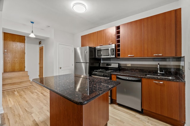 kitchen with stainless steel appliances, dark stone countertops, sink, hanging light fixtures, and light hardwood / wood-style flooring