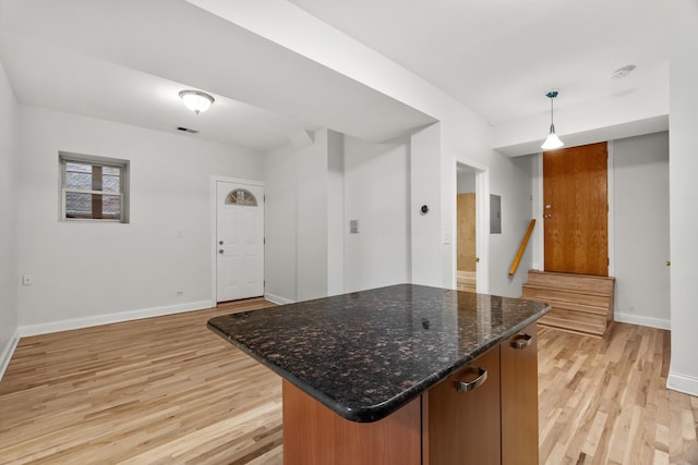 kitchen with hanging light fixtures, dark stone countertops, light hardwood / wood-style flooring, and a kitchen island