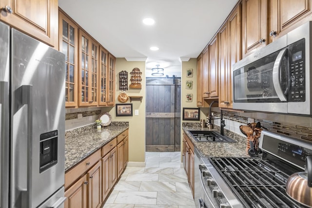 kitchen with sink, appliances with stainless steel finishes, tasteful backsplash, a barn door, and dark stone counters