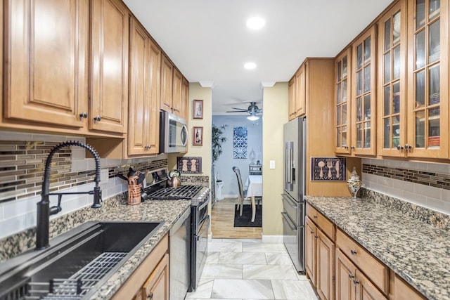 kitchen featuring sink, stone countertops, appliances with stainless steel finishes, ceiling fan, and backsplash