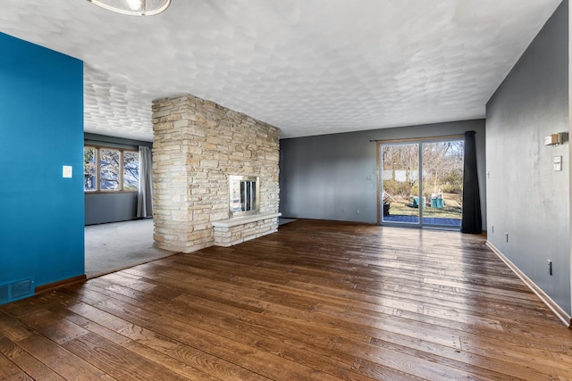 unfurnished living room with a textured ceiling, hardwood / wood-style floors, and a stone fireplace