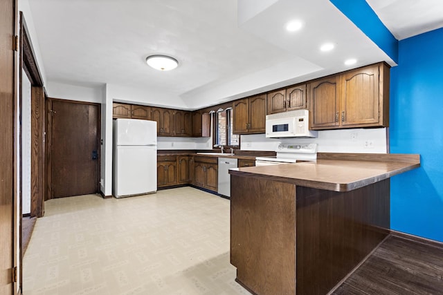 kitchen with kitchen peninsula, white appliances, a kitchen breakfast bar, dark brown cabinets, and sink