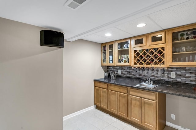 bar featuring a paneled ceiling, dark stone counters, decorative backsplash, sink, and light tile patterned floors