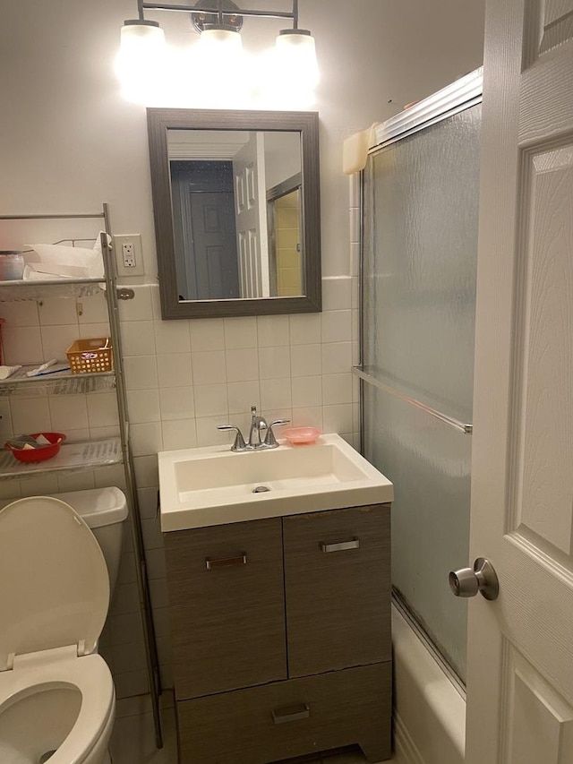 full bathroom with combined bath / shower with glass door, tile walls, decorative backsplash, vanity, and toilet