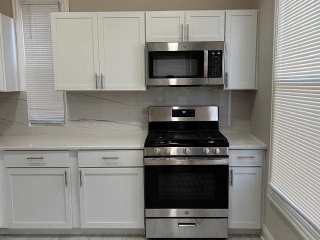 kitchen featuring stainless steel appliances, decorative backsplash, white cabinets, and light stone counters